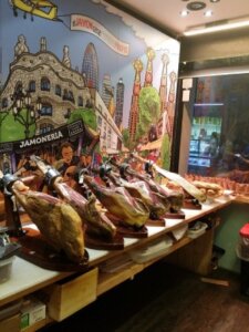 A hotel intern buying fresh jamón slices directly from a jamón leg at a local market in Spain.