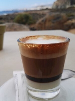 Un stagista in hotel gustando un bicchiere di leche leche, una bevanda spagnola dolce a base di latte condensato e caffè, durante una pausa nella sua formazione pratica in Spagna.